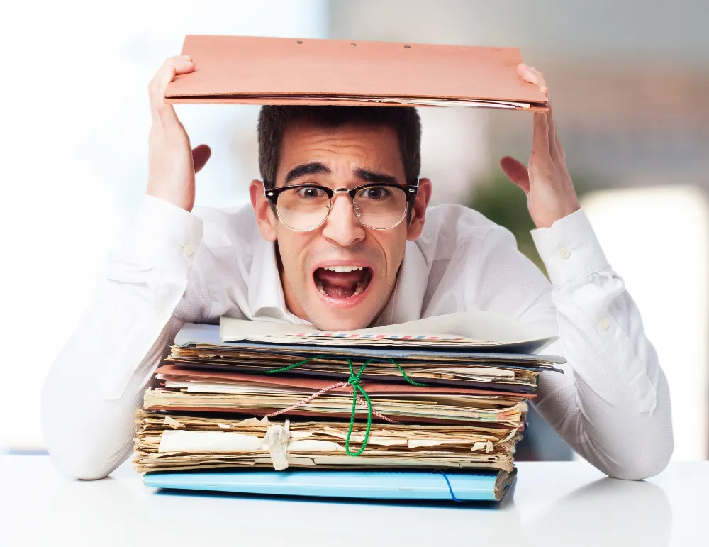 Homme anxieux seul face à une pile de documents anciens à traiter risquant des maladies psychosociaux.