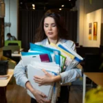 Femme en train de porter des piles de chemises dossier et de classeur encourant une chute faisant partie des risques du métier archiviste